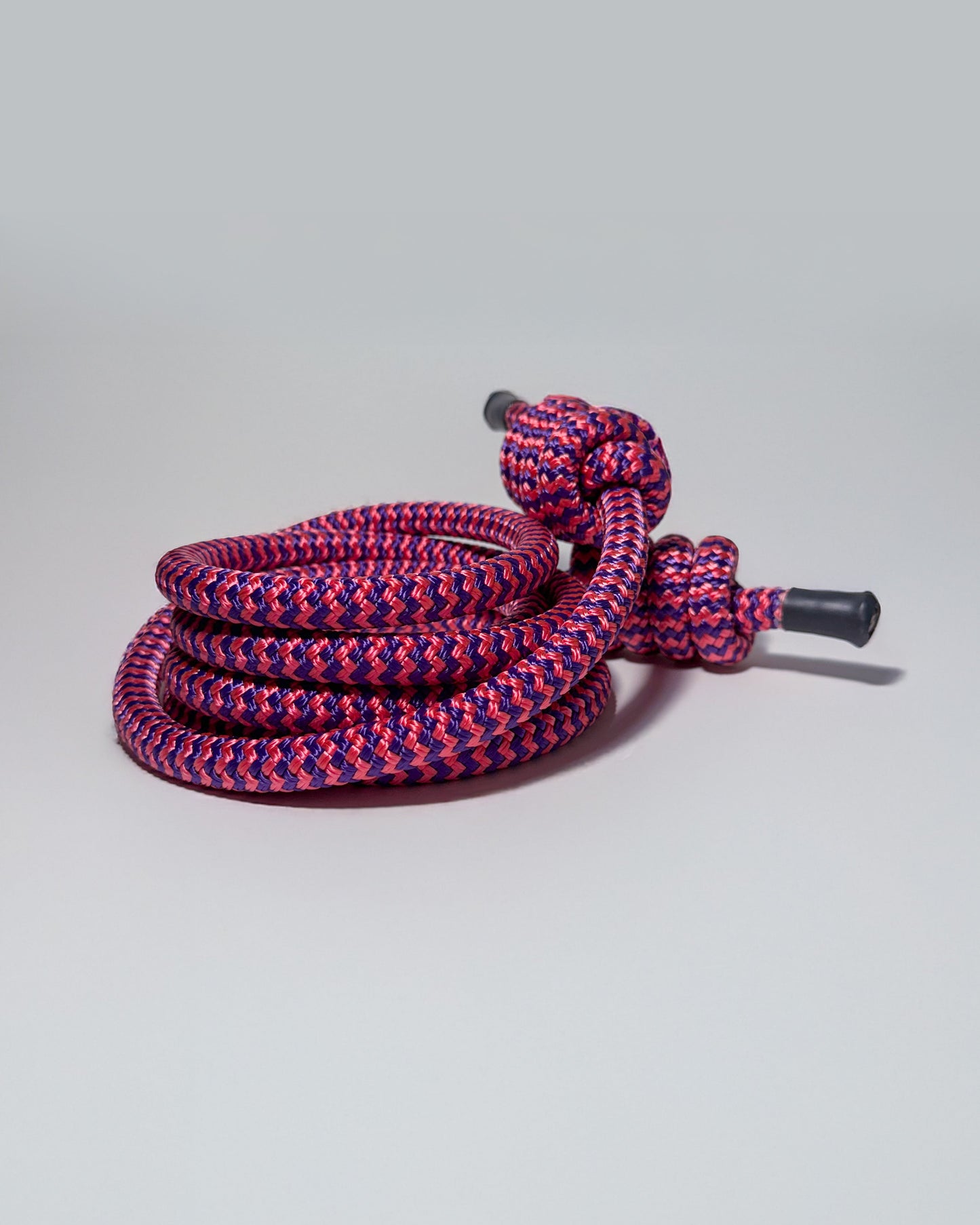 Purple and pink braided rope with black ends on a gray background