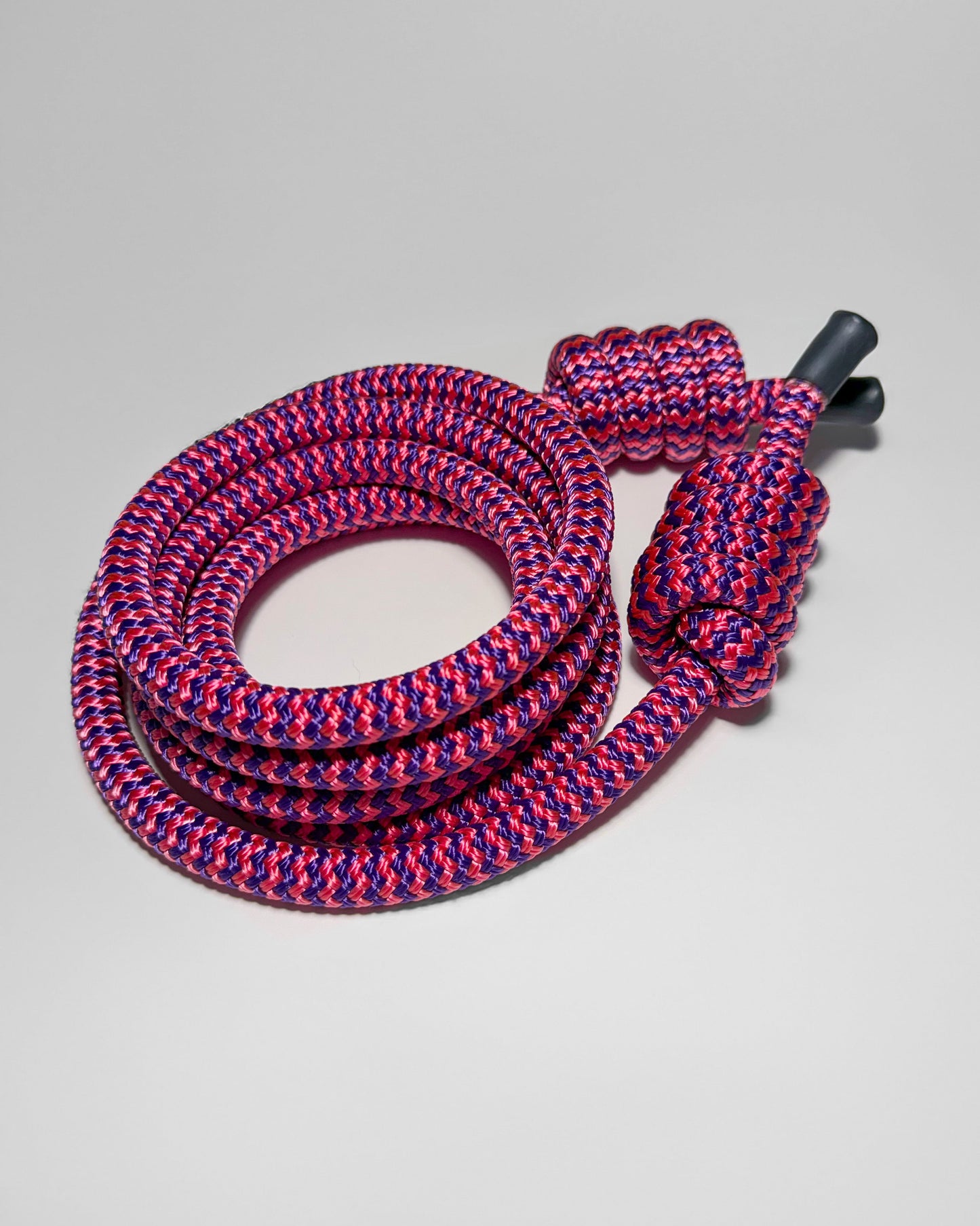 Coiled pink and purple flow rope with a black end cap on a light gray background