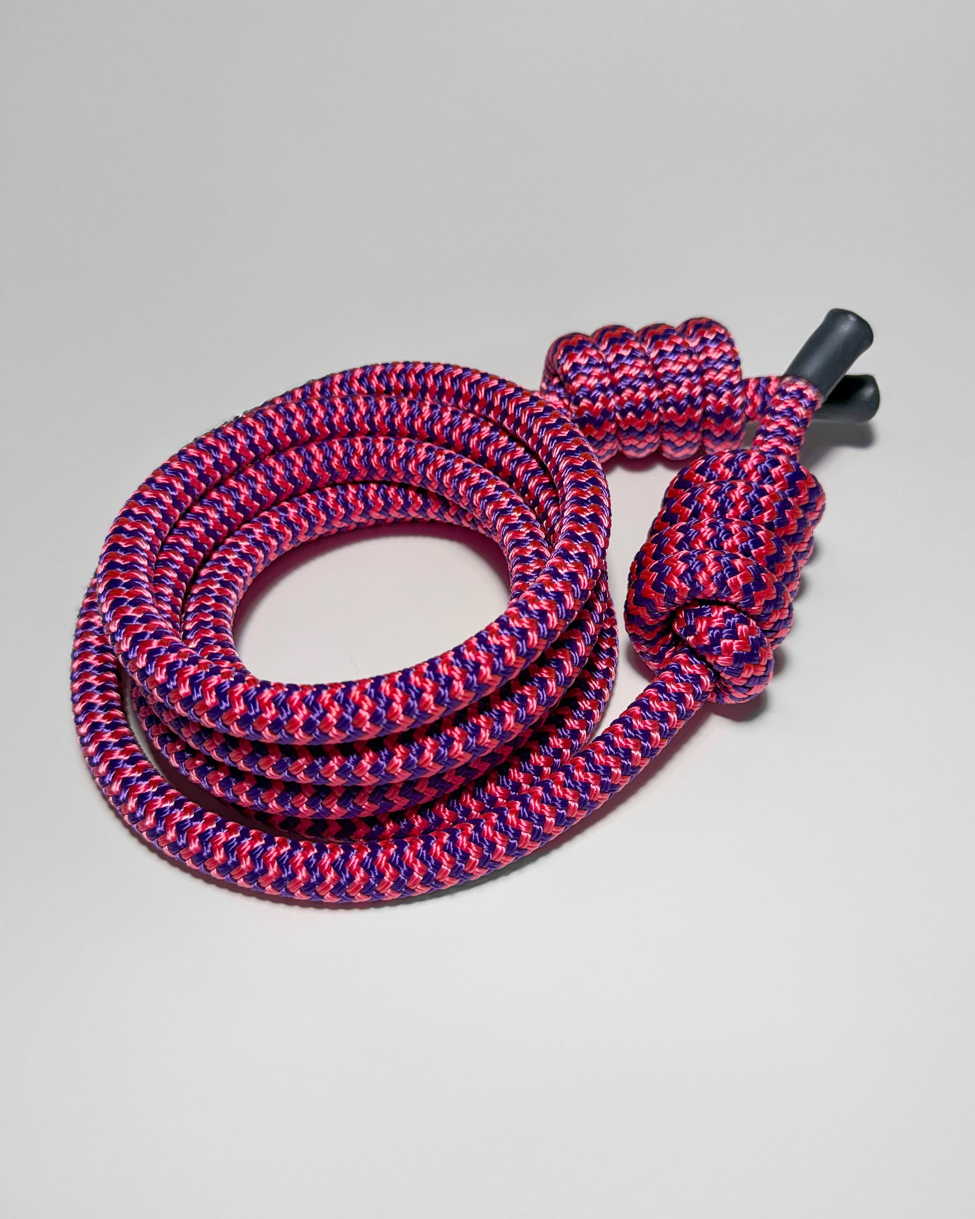 Coiled pink and purple flow rope with a black end cap on a light gray background