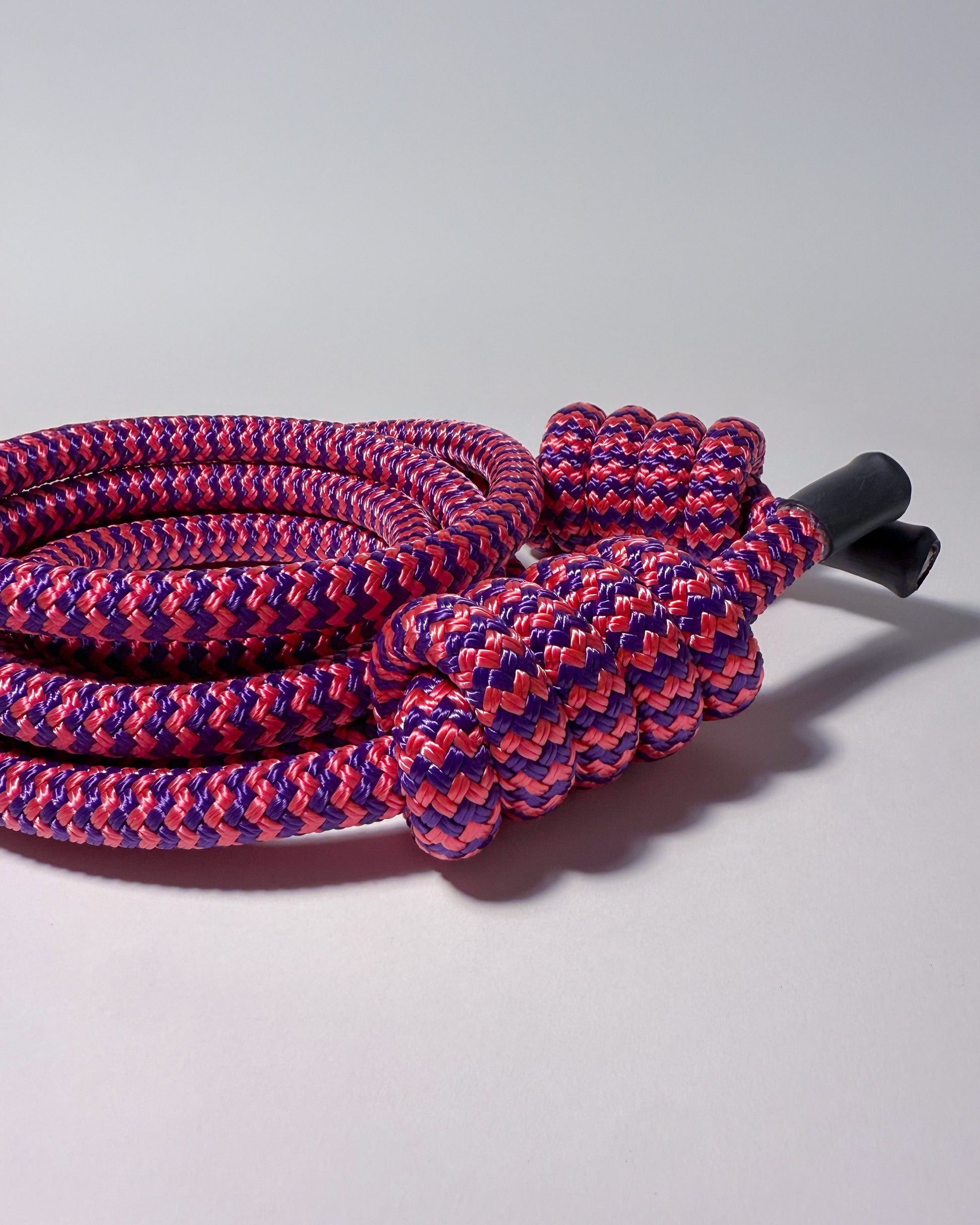 Coiled pink and purple rope with a black end cap on a light gray background